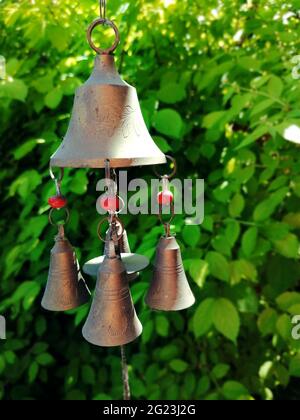 Autentico campanello di ottone contro foglie verdi di un cespuglio. Fotografia mobile. Illustrazione per la stagione estiva di giardinaggio. Foto Stock