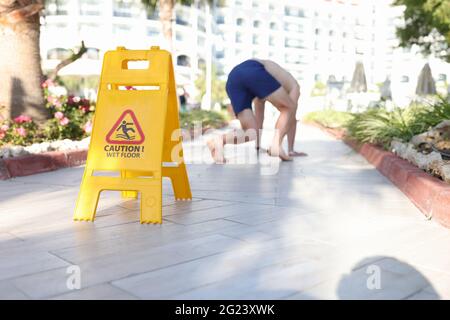 Uomo che cade su piastrella vicino segno con iscrizione attenzione pavimento bagnato closeup Foto Stock