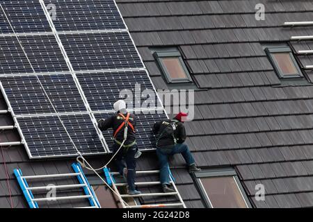 Operai edili che installano pannelli solari sui tetti di case di nuova costruzione Foto Stock