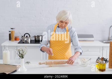Donna anziana che versa la farina sul tondino in cucina Foto Stock