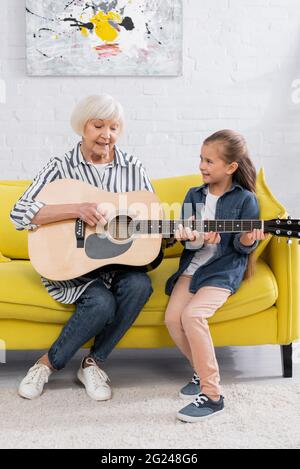 Nonna allegra e capretto che suonano chitarra acustica sul divano Foto Stock