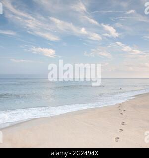 USA, Massachusetts, Cape Cod, Nantucket Island, impronte sulla spiaggia e donna che nuota in mare in lontananza Foto Stock