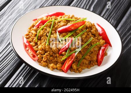 La gustosa varietà di curry secco del sud della Thailandia di Khua Kling combina pasta di curry piccante e maiale macinato da vicino nel piatto sul tavolo. Orizzontale Foto Stock