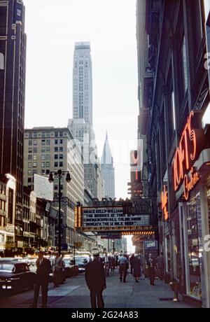 Guardando se lungo West 42nd Street, New York City, Stati Uniti nel 1955. Il Bryant Theatre mostra ‘i ponti di Toko-Ri’, un film della guerra coreana con Grace Kelly e William Holden. In lontananza si trova il famoso grattacielo art deco Chrysler Building. Luminoso e illuminato da neon, è il fulcro del quartiere dei teatri di Broadway. Questa immagine proviene da una vecchia trasparenza dei colori Kodak scattata da un fotografo dilettante – una fotografia degli anni '50. Foto Stock