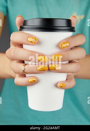 Mani donne con manicure arancione alla moda che tiene la tazza di carta Foto Stock
