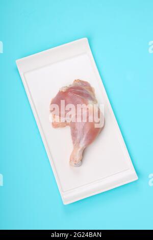 Coscia di pollo intera grezza senza pelle sistemata a forma rettangolare piatti con fondo di colore pieno blu ghiaccio Foto Stock