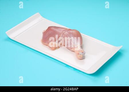 Coscia di pollo intera grezza senza pelle sistemata a forma rettangolare piatti con fondo di colore pieno blu ghiaccio Foto Stock