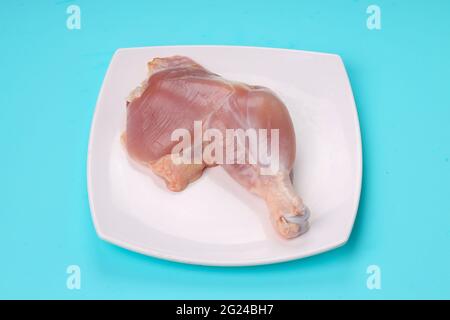 Gamba intera di pollo cruda senza pelle disposta in una tavola bianca di forma quadrata con fondo di colore pieno blu ghiaccio. Foto Stock