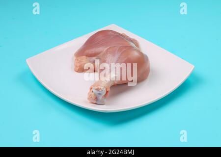 Gamba intera di pollo cruda senza pelle disposta in una tavola bianca di forma quadrata con fondo di colore pieno blu ghiaccio. Foto Stock