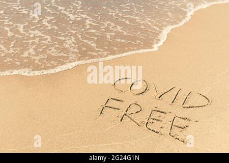 Covid libero scritto sulla riva, sulla sabbia di una spiaggia con onda che lava la parola, cancellandola o cancellandola durante l'estate di Coronavirus, Covid libero Foto Stock
