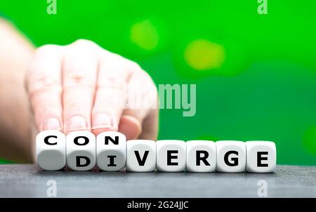 La mano trasforma i dadi e cambia la parola "Deverge" in "converge". Foto Stock