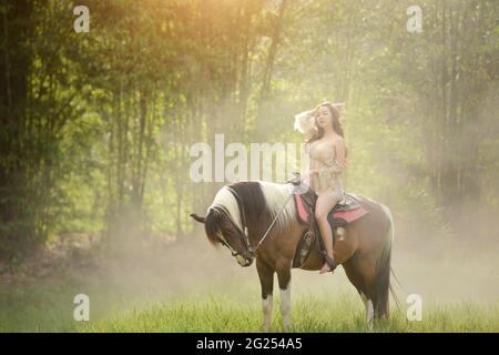 Donna seduta su un cavallo in un campo, Thailandia Foto Stock