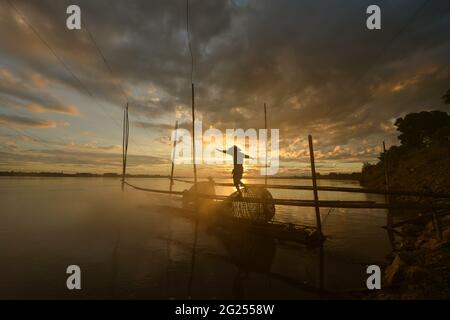 Silhouette di un pescatore che cammina lungo un molo al tramonto, Thailandia Foto Stock