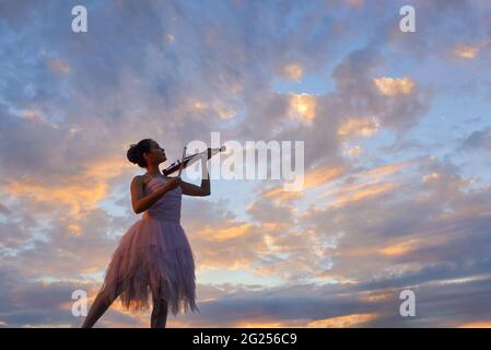 Donna in piedi all'aperto al tramonto che suona il violino, Thailandia Foto Stock