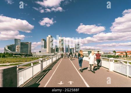 Vilnius, Lituania - 30 maggio 2021: Persone a piedi, in bicicletta e scooter sul ponte bianco. Paesaggio urbano di Vilnius con il fiume Neris Foto Stock