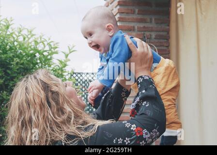 Donna sorridente in piedi nel giardino che tiene il suo bambino nell'aria Foto Stock