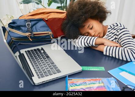 La piccola studentessa si addormentò durante l'apprendimento online a casa, mise la testa riccia sul tavolo della scuola dopo una lezione dura, e si riposa Foto Stock