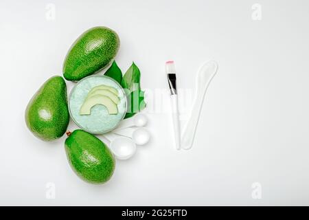 Cosmetici naturali cura della pelle del viso in avocado. Maschera di frutta all'avocado. Set di strumenti per la produzione di cosmetici per la casa. Piatto su sfondo bianco con Foto Stock