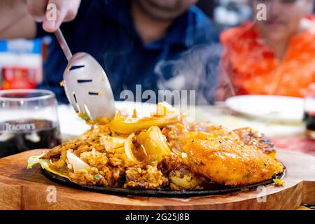 giovane coppia persone raccogliere oggetti da un piatto di casa cotto sizzler con principianti, patate e pollo di carne con il fuoco sul piatto con Foto Stock