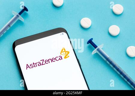 Galizia, Spagna; 8 Giugno 2020 : smartphone con logo AstraZeneca sullo schermo e pillole e siringa su sfondo blu Foto Stock