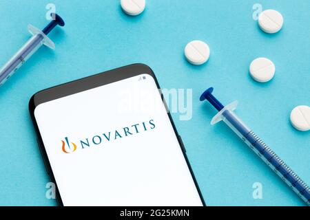Galizia, Spagna; 8 Giugno 2020 : smartphone con logo Novartis sullo schermo e pillole e siringa su sfondo blu Foto Stock