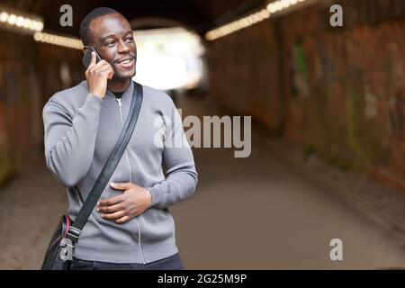 Sorridente giovane uomo in ambiente urbano in piedi in Tunnel che parla sul telefono cellulare Foto Stock