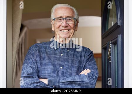 Ritratto di sorridente uomo anziano in piedi alla porta aperta della casa Foto Stock