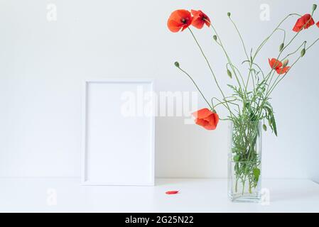 Immagine vuota bianco mockup cornice. Vaso di vetro con bellissimi fiori di papavero selvatico su tavolo bianco. Vivace e allegra scena di vita still estiva. Buon giorno Foto Stock