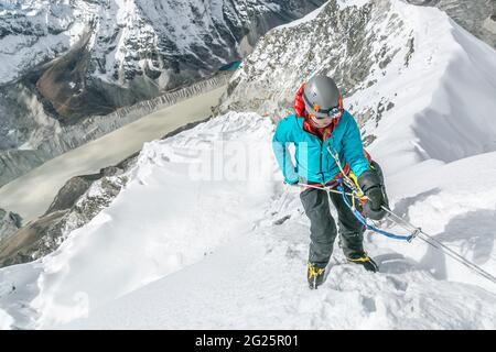 Donna alpinista con grandi mittens in procinto di iniziare la discesa della testiera Foto Stock