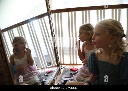 due ragazze piccole che guardano nello specchio che mettono sul rossetto Foto Stock