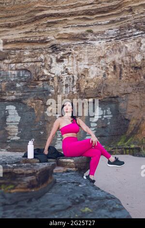 Donna in outfit da allenamento seduta su una roccia vicino alle scogliere. Foto Stock