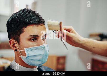 un ragazzo con una maschera facciale gli fa spazzolarsi i capelli nel barbiere Foto Stock