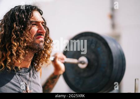 Uomo dai capelli lunghi con faccia sofferente che tiene i manubri Foto Stock