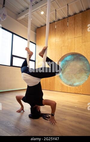 Giovane donna tutta in nero che fa yoga aereo allo studio di legno in Messico Foto Stock