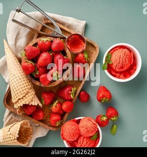 Sorbetto alla fragola con fragole su sfondo blu con spazio per la copia. Un mucchio di fragola con gelato in tazze di carta. Foto Stock