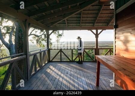 Un uomo anziano su una grande veranda si prende nel bellissimo paesaggio di una palude di sale di bassa campagna all'alba vicino all'isola di Sapelo, Georgia costiera, Stati Uniti. Foto Stock