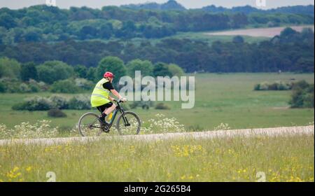 Il ciclista che indossa una giacca ad alta visibilità su una pedalata si fa strada attraverso una pista di pietra nell'area di addestramento militare di Salisbury Plain Foto Stock