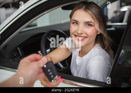 Bella donna felice seduta nella sua nuova automobile, ricevendo le chiavi dell'automobile dal venditore Foto Stock