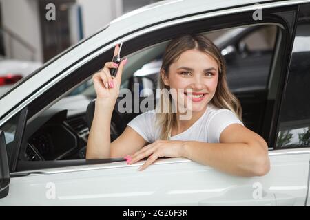 Bella donna allegra che tiene le chiavi dell'automobile, seduta nella sua nuova automobile Foto Stock