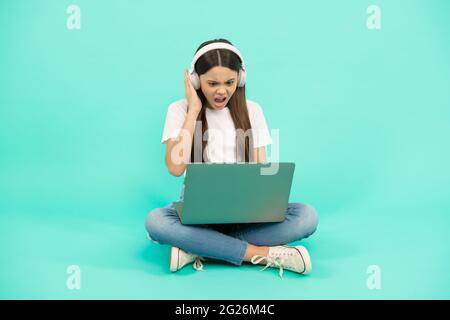 scioccato bambino ragazza influencer utilizzare il computer per videochiamata o ascoltare webinar in cuffia, blogging. Foto Stock