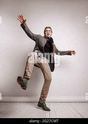 L'uomo adulto in pantaloni e giacca di plaid sta tenendo il piede in su, facendo il passo gigante, cadendo giù le mani che ondolano Foto Stock