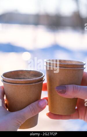 Mano di donne con tazza di carta di caffè in fondo neve invernale. Tazze monouso in carta marrone scuro. Caffè da portare via. Pausa caffè Foto Stock