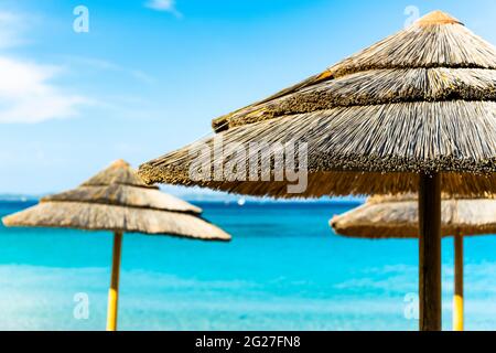 (Fuoco selettivo) splendida vista di un ombrello di paglia in primo piano e bellissimo mare turchese sullo sfondo. Sardegna, Italia. Foto Stock