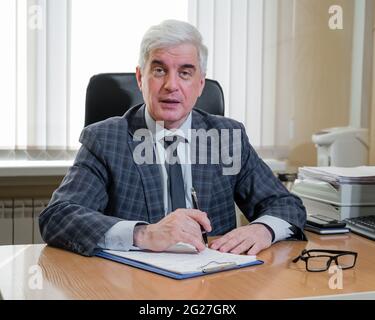 Un uomo anziano sicuro con capelli grigi in una tuta a si siede alla sua scrivania in ufficio Foto Stock