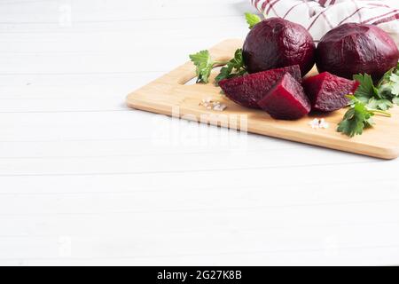 Barbabietole bollite intere e tagliate su un tagliere con foglie di prezzemolo su fondo bianco. Spazio di copia, Foto Stock
