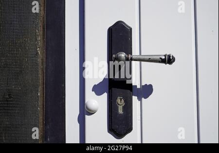 Vecchia maniglia in metallo nero su una porta di legno bianco. Primo piano dello sportello bloccato con foro per chiave. Foto Stock