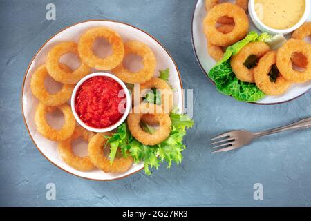 Anelli di calamari. Anelli di calamari fritti profondi con lattuga e varie salse, sopra un piano di posa su sfondo blu Foto Stock