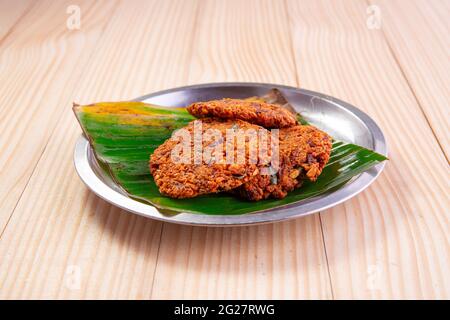 Parippu vada o Lentil Fritters, disposti tradizionalmente in una piastra d'acciaio rivestita con foglia di banana con fondo testurizzato in legno. Foto Stock