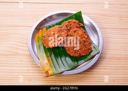 Parippu vada o Lentil Fritters, disposti tradizionalmente in una piastra d'acciaio rivestita con foglia di banana con fondo testurizzato in legno. Foto Stock