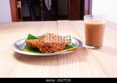 Parippu vada o Lentil Fritters, disposti tradizionalmente in una piastra di acciaio rivestita con foglia di banana e un bicchiere di tè accanto ad esso con legno testurizzato bac Foto Stock